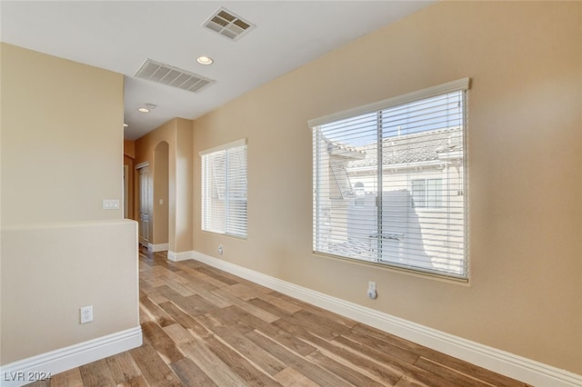 unfurnished room featuring visible vents, arched walkways, light wood-style floors, and baseboards