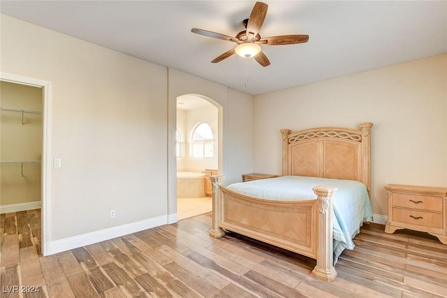 bedroom with baseboards, ensuite bath, light wood-style flooring, arched walkways, and a spacious closet