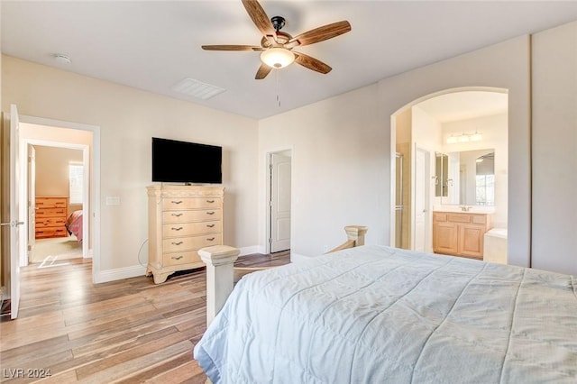 bedroom with a ceiling fan, connected bathroom, arched walkways, light wood-style floors, and baseboards