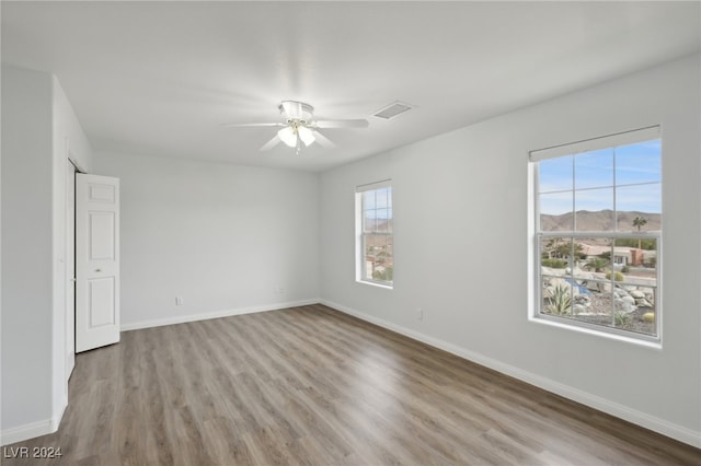 empty room with a mountain view, light hardwood / wood-style flooring, and ceiling fan