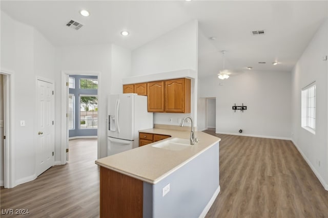 kitchen with sink, white fridge with ice dispenser, high vaulted ceiling, kitchen peninsula, and light wood-type flooring