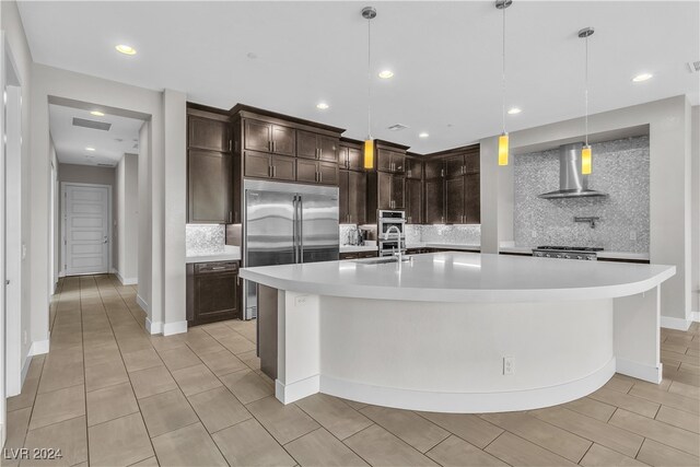 kitchen featuring pendant lighting, tasteful backsplash, a spacious island, and wall chimney range hood