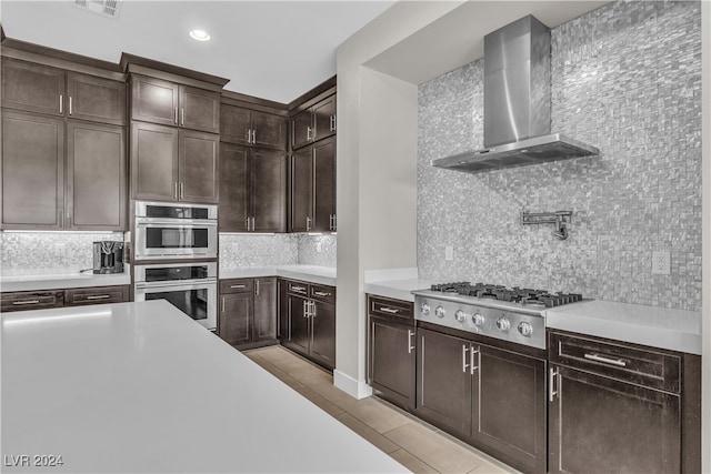 kitchen with stainless steel gas stovetop, backsplash, wall chimney range hood, light tile patterned floors, and dark brown cabinetry