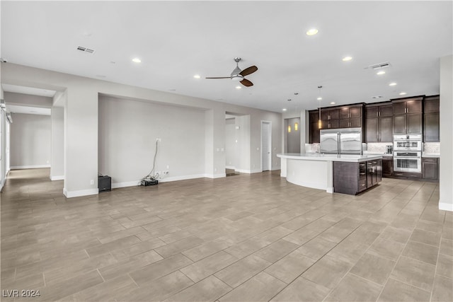 kitchen with ceiling fan, an island with sink, decorative light fixtures, dark brown cabinetry, and stainless steel appliances