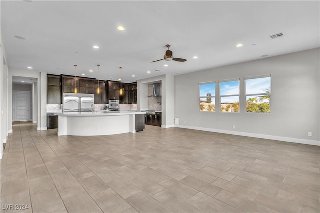 kitchen featuring ceiling fan, stainless steel appliances, an island with sink, decorative light fixtures, and decorative backsplash