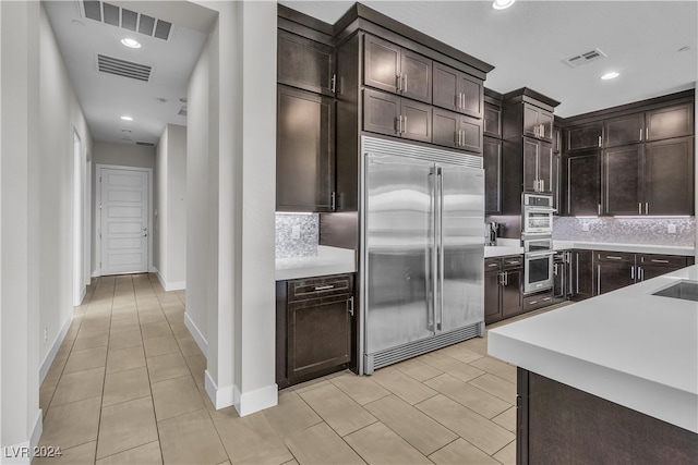 kitchen with tasteful backsplash, dark brown cabinetry, stainless steel built in fridge, and light tile patterned floors