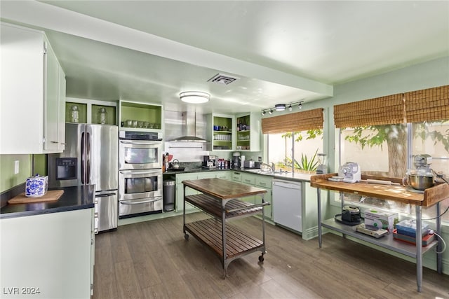 kitchen featuring sink, stainless steel appliances, wall chimney range hood, dark hardwood / wood-style floors, and white cabinets