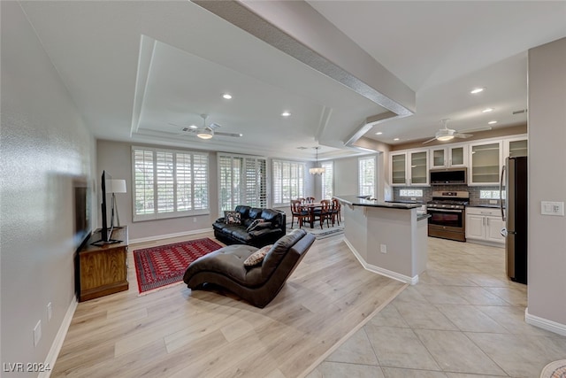 living room with a raised ceiling, ceiling fan, and light hardwood / wood-style flooring