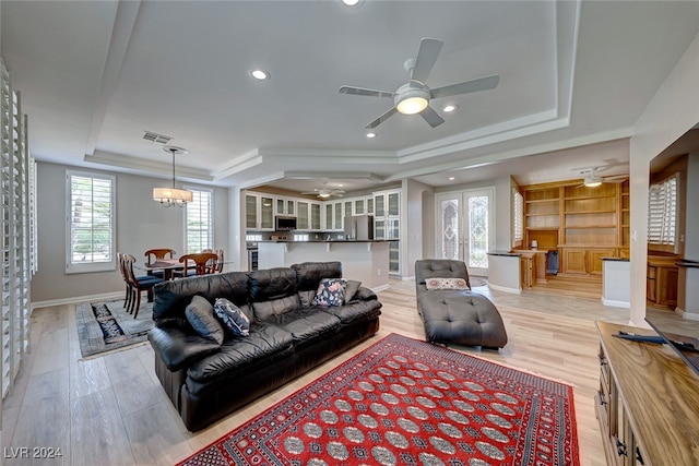 living room with ceiling fan with notable chandelier, a raised ceiling, light wood-type flooring, and a wealth of natural light