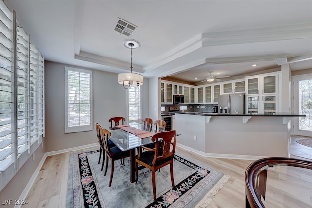 dining room featuring a tray ceiling, ceiling fan with notable chandelier, and light wood-type flooring