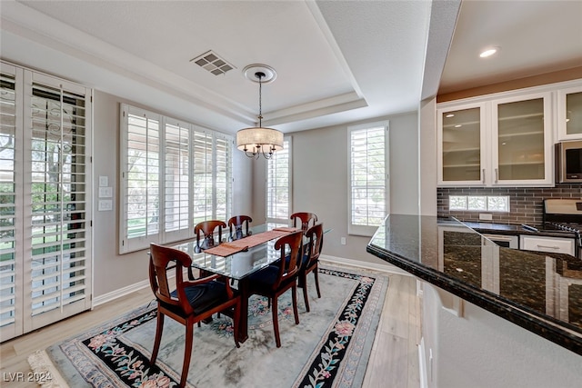 dining room with light hardwood / wood-style floors, a tray ceiling, and an inviting chandelier