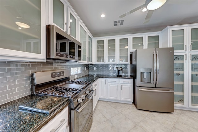 kitchen featuring white cabinetry, stainless steel appliances, backsplash, dark stone countertops, and light tile patterned floors