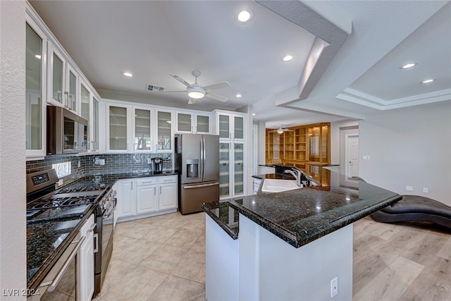 kitchen with stainless steel appliances, dark stone counters, a breakfast bar area, decorative backsplash, and white cabinets