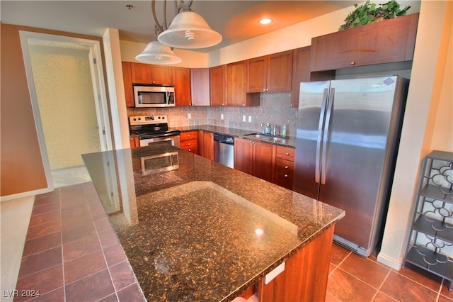 kitchen featuring sink, hanging light fixtures, dark stone counters, decorative backsplash, and appliances with stainless steel finishes