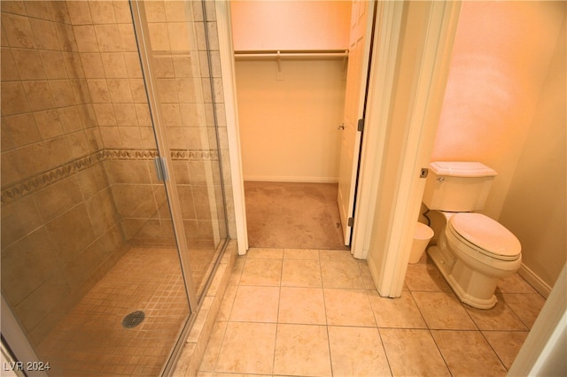 bathroom with tile patterned floors, toilet, and a shower with door