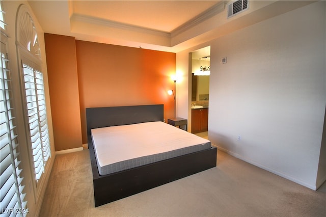 bedroom with connected bathroom, light colored carpet, a raised ceiling, and ornamental molding