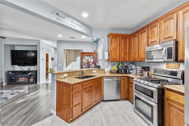 kitchen featuring light stone countertops, sink, kitchen peninsula, appliances with stainless steel finishes, and light wood-type flooring