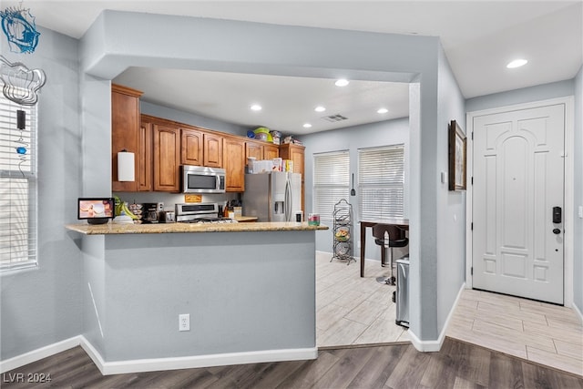 kitchen featuring light hardwood / wood-style floors, light stone countertops, kitchen peninsula, and stainless steel appliances