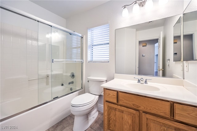 full bathroom with combined bath / shower with glass door, tile patterned floors, vanity, and toilet