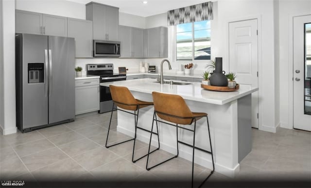 kitchen featuring a kitchen island with sink, sink, light tile patterned flooring, a kitchen bar, and stainless steel appliances