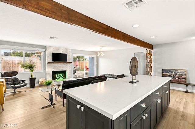 kitchen featuring a healthy amount of sunlight, beam ceiling, a center island, and a brick fireplace