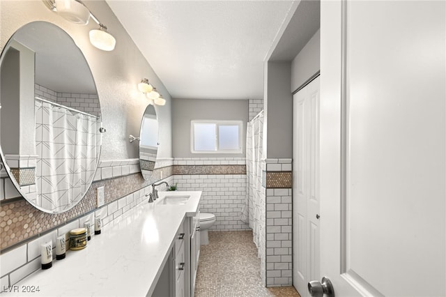 bathroom featuring vanity, toilet, tile walls, and a textured ceiling