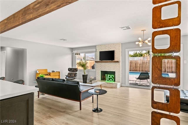 living room with a brick fireplace, plenty of natural light, a chandelier, and light wood-type flooring