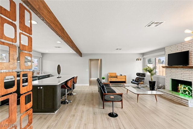 living room with a brick fireplace, beam ceiling, and light hardwood / wood-style flooring