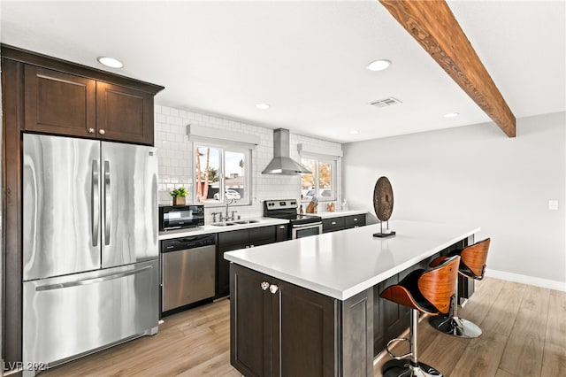 kitchen featuring sink, a breakfast bar area, appliances with stainless steel finishes, a kitchen island, and wall chimney exhaust hood