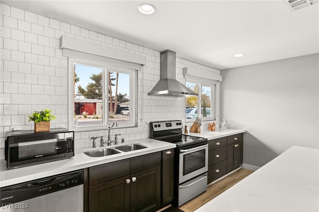 kitchen featuring appliances with stainless steel finishes, sink, decorative backsplash, dark brown cabinets, and wall chimney range hood