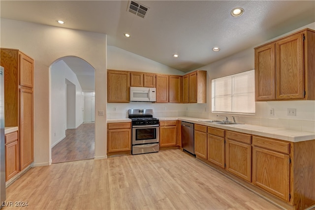 kitchen with lofted ceiling, sink, light hardwood / wood-style flooring, appliances with stainless steel finishes, and tile counters