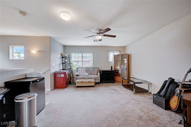 living area with a textured ceiling, light colored carpet, and ceiling fan