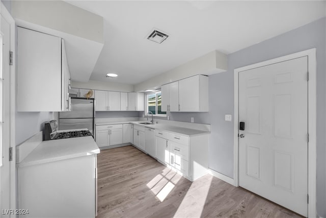 kitchen with appliances with stainless steel finishes, light hardwood / wood-style flooring, white cabinetry, and sink