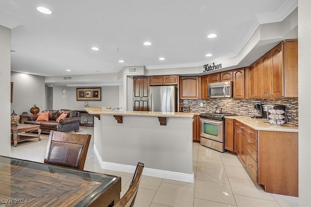 kitchen with decorative backsplash, light tile patterned floors, ornamental molding, appliances with stainless steel finishes, and a breakfast bar area