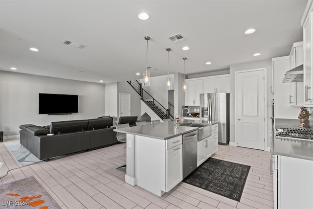 kitchen featuring stainless steel appliances, a kitchen island with sink, light hardwood / wood-style flooring, white cabinetry, and hanging light fixtures