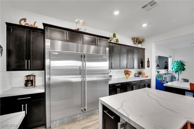 kitchen with built in fridge, a kitchen island, tasteful backsplash, light hardwood / wood-style floors, and light stone counters