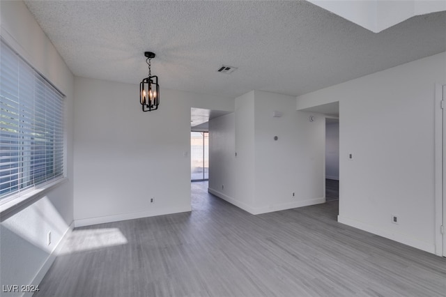 spare room with a textured ceiling, light hardwood / wood-style flooring, and a notable chandelier