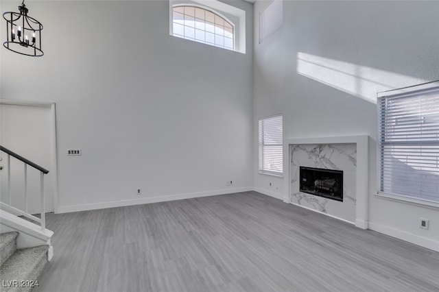 unfurnished living room with a high ceiling, a high end fireplace, a chandelier, and light hardwood / wood-style floors