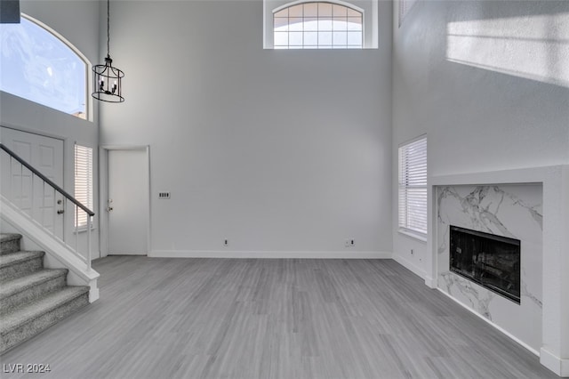 unfurnished living room with a high ceiling, wood-type flooring, a fireplace, and a chandelier