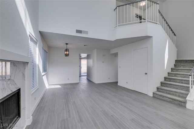 unfurnished living room featuring a notable chandelier, light hardwood / wood-style flooring, and a high ceiling