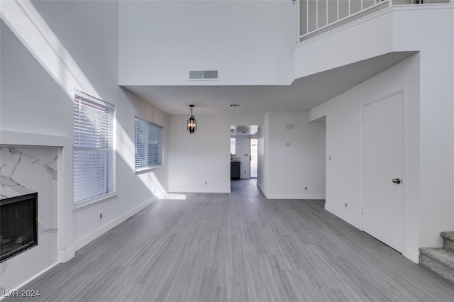 unfurnished living room with a high ceiling, a high end fireplace, and light wood-type flooring