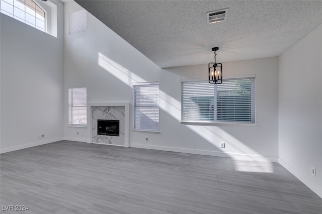 unfurnished living room featuring an inviting chandelier, hardwood / wood-style floors, a textured ceiling, and a high end fireplace