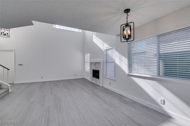 unfurnished living room with a high end fireplace, light hardwood / wood-style floors, a textured ceiling, and a notable chandelier