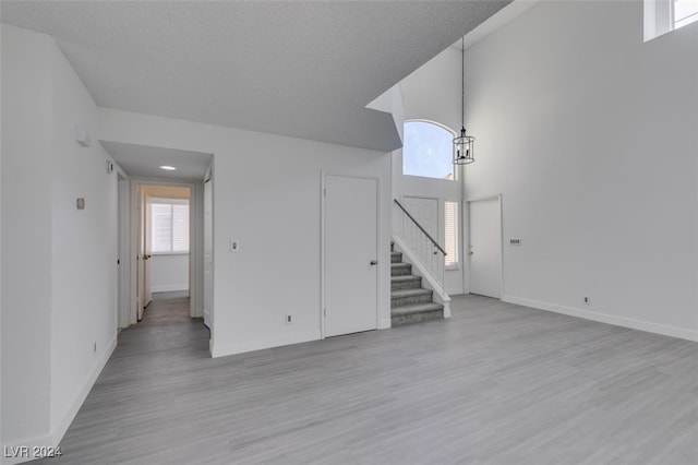 unfurnished living room with light hardwood / wood-style flooring, a textured ceiling, and a high ceiling