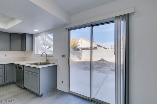 kitchen with gray cabinets, dishwashing machine, sink, and light hardwood / wood-style flooring