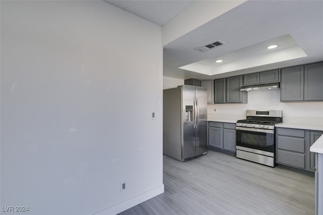 kitchen with appliances with stainless steel finishes, a raised ceiling, light wood-type flooring, and gray cabinetry