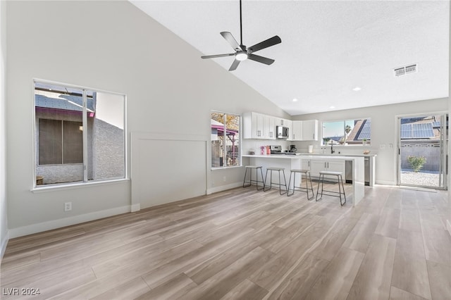 unfurnished living room featuring ceiling fan, high vaulted ceiling, and light wood-type flooring