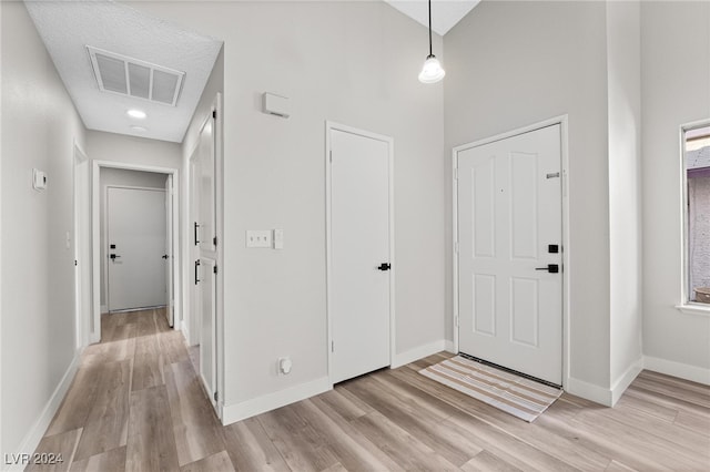 foyer entrance with a towering ceiling, a textured ceiling, and light hardwood / wood-style flooring