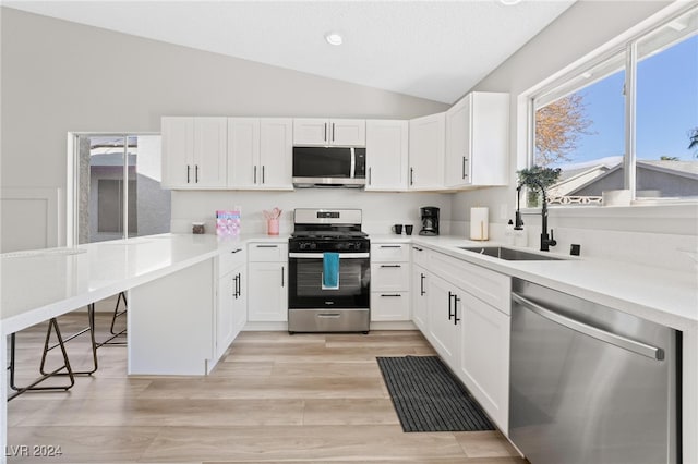 kitchen with appliances with stainless steel finishes, light wood-type flooring, sink, white cabinetry, and lofted ceiling