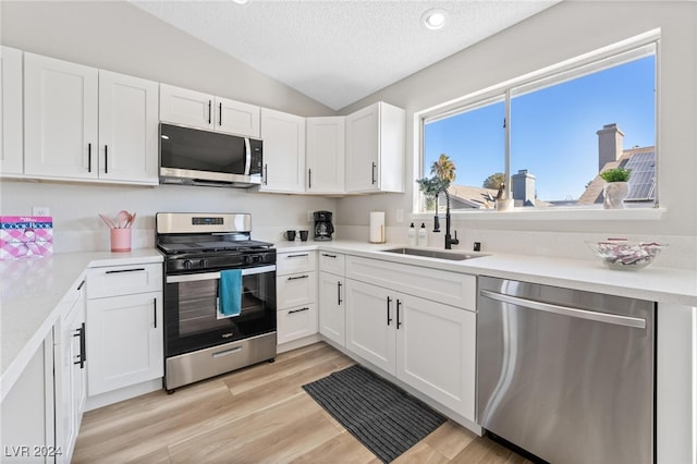 kitchen with appliances with stainless steel finishes, light wood-type flooring, sink, white cabinets, and lofted ceiling